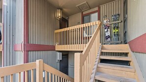 A wooden staircase leading to a balcony with a railing, a door, and a wall with vertical panels. - Mountain Charmer | Steps to Main St & Trails (Frisco)