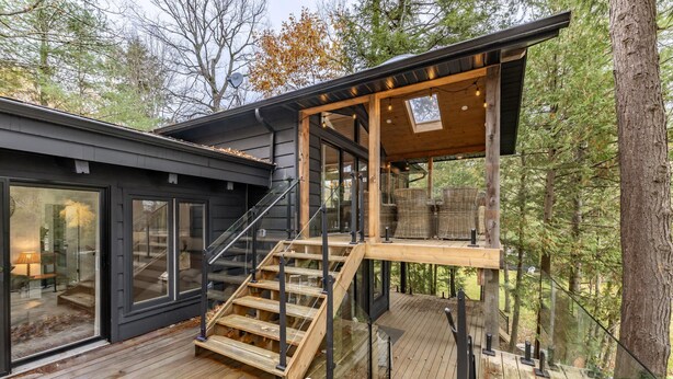 A modern wooden deck with glass railings, a staircase, and a covered outdoor seating area. - Delightful 4 bed 2 bath on Bass Lake (MacTier)