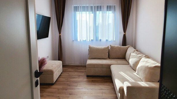 Una sala de estar moderna con un conjunto de sofá, un televisor de pantalla plana montado en la pared y un ventanal con cortinas translúcidas.