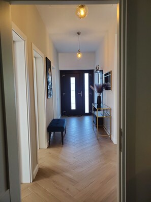 Um corredor com piso de madeira, um banco, uma porta e uma prateleira fixada na parede.