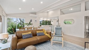A spacious living area with a brown sofa, a blue armchair, and a dining area with wooden chairs. - Strandhus in Mollymoook (Mollymook Beach)