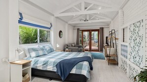 A bedroom with a bed, bedside tables, a window with curtains, a ceiling fan, and a view of the outdoors. - Strandhus in Mollymoook (Mollymook Beach)