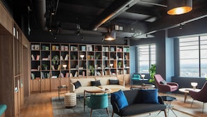 A modern interior with a large bookshelf, comfortable seating, and large windows offering a view. - Enclave Croydon - Campus Accommodation (Croydon)