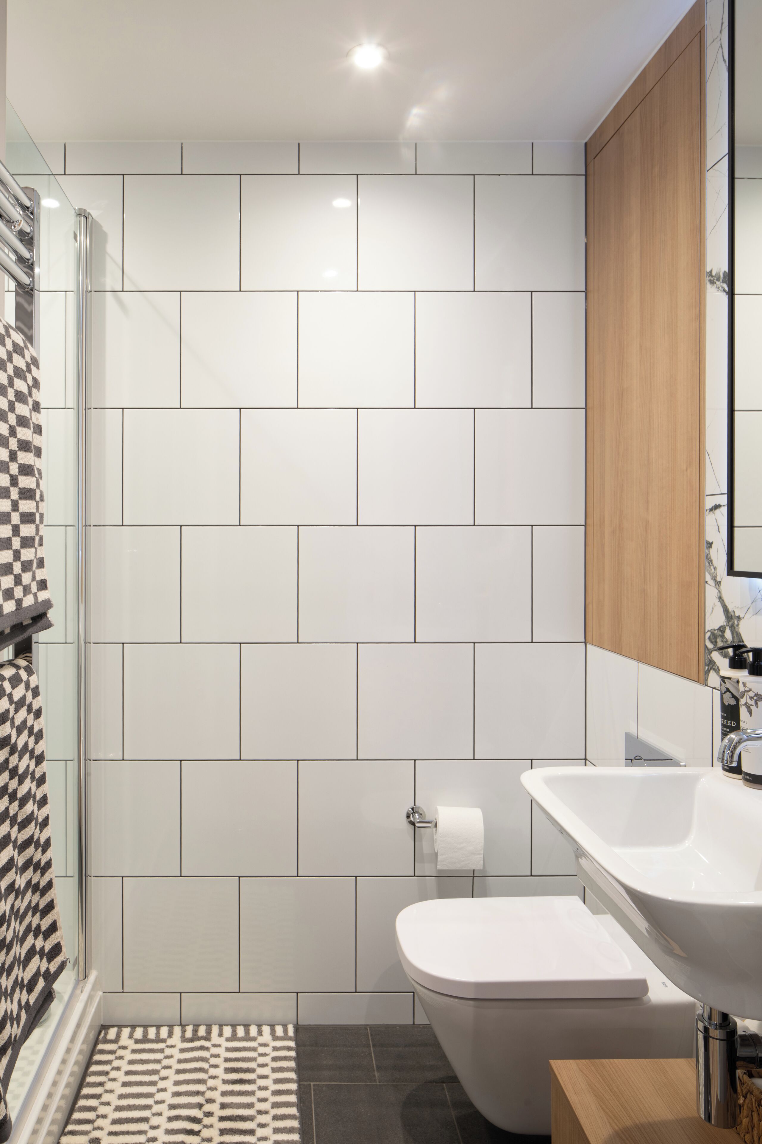 Un baño moderno con azulejos blancos, un mueble de madera, un lavamanos y un inodoro.
