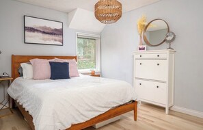 A bedroom with a wooden bed, white dresser, and a large window. - Delightful apartment with AC in charming Lake Oswego (Lake Oswego)