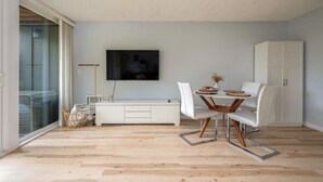 Una sala de estar moderna con televisor de pantalla plana, muebles blancos y un gran ventanal corredizo.