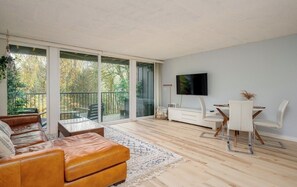 Moderni olohuone, jossa on sohva, ruokapöytä tuoleineen, seinälle asennettu televisio ja lasiovilla varustettu parveke.