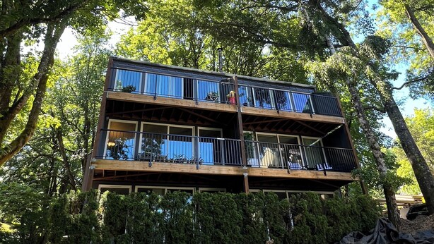 Una cabaña de madera de varios pisos con balcones, rodeada de árboles.