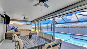 A covered outdoor area with a pool, seating, and a TV. - 419 El Dorado Pkwy W (Cape Coral)