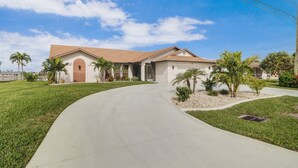 A single-story house with a curved driveway, a garage, and a small front yard with palm trees and shrubs. - 419 El Dorado Pkwy W (Cape Coral)