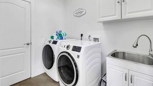 A laundry room with two front-loading washing machines, a sink, and a sign above the machines. - 4213 SW 26th Ave (Cape Coral)