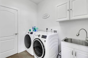 A laundry room with two front-loading washing machines, a sink, and a sign above the machines. - 4213 SW 26th Ave (Cape Coral)