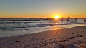 Ein Strand mit einer hölzernen Pier, die sich in den Ozean erstreckt, bei Sonnenuntergang.