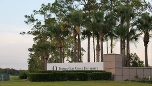 Schild der Florida Gulf Coast University, im Hintergrund eine Rasenfläche und Palmen.