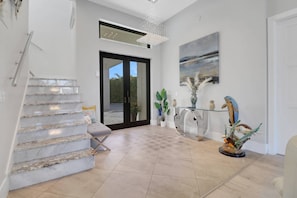 A modern interior with a staircase, a glass coffee table, and a painting on the wall. - 2416 SW 49th Ter (Cape Coral)
