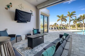 A modern outdoor living area with a sofa, a table, and a TV mounted on the wall. - 2416 SW 49th Ter (Cape Coral)