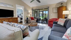 A living room with a television, sofa, and chairs, a ceiling fan, and a view through a glass door. - 11961 Caraway Ln #87 (Fort Myers)
