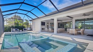 A modern indoor swimming pool with glass walls, a sun terrace with outdoor furniture, and a clear view of the surrounding greenery. - 2301 SW 39th St (Cape Coral)
