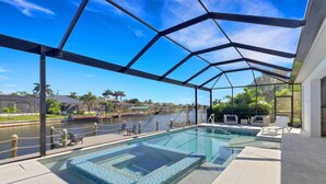 A pool area with a glass enclosure, clear water, and a view of a body of water and buildings in the background. - 2301 SW 39th St (Cape Coral)