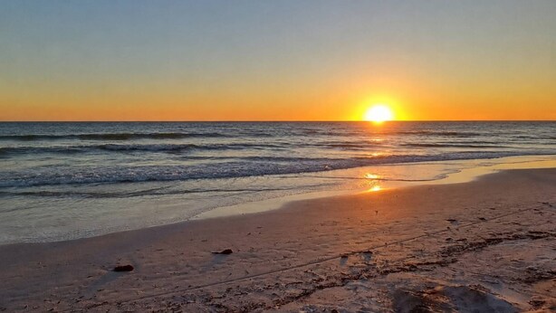 A beach with the sun setting over the ocean, calm waves, and a sandy shore. - 2301 SW 39th St (Cape Coral)