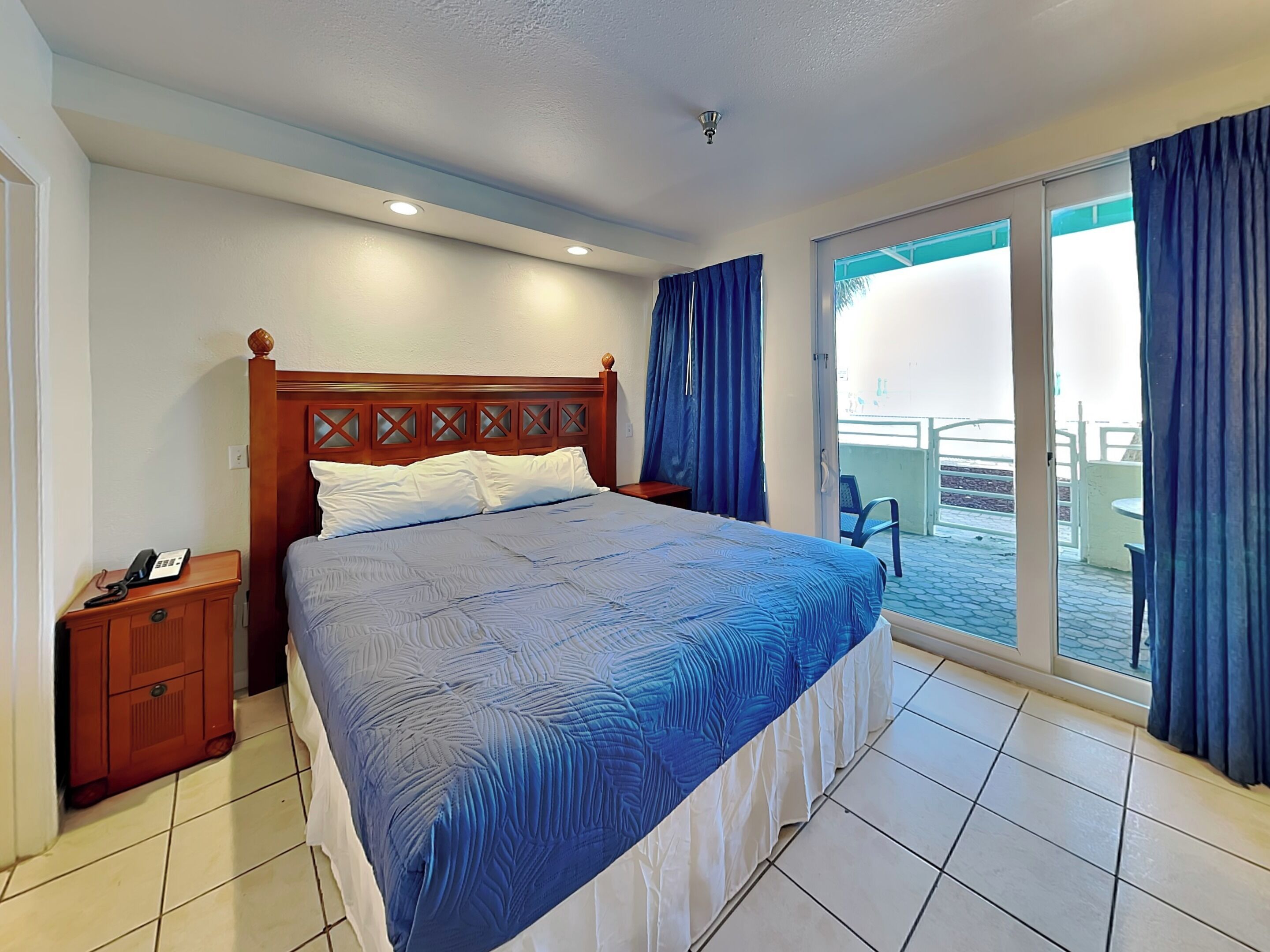 A hotel room with a bed, a nightstand, a telephone, and a view of the outside balcony.
