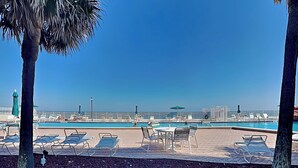 A poolside area with lounge chairs and umbrellas, a clear sky, and a distant cityscape. - Harbour Beach Resort 103 (Daytona Beach)