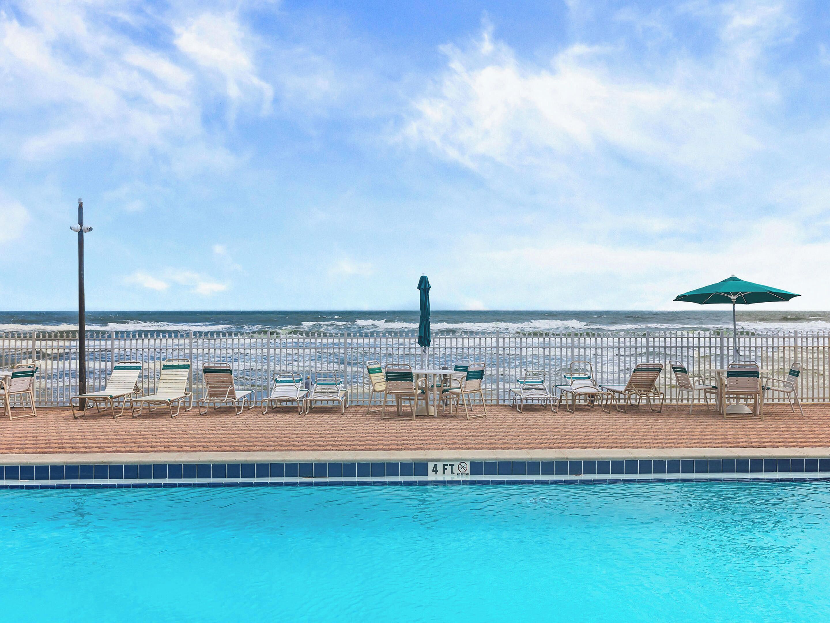 A poolside area with lounge chairs and a view of the ocean.