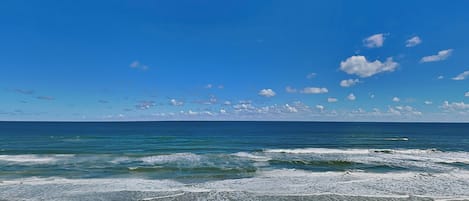 Una playa con cielo despejado, olas y sombrillas.