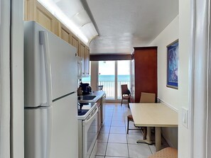 Eine kleine Küche mit Kühlschrank, Herd und Spüle, die zu einem Balkon mit Meerblick führt.