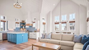 A spacious living area with a large sofa and a coffee table, a kitchen with blue cabinets and a central island, and a dining area with a table and chairs. - Beaches and Cream 210 DEW (Port Aransas)