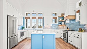 A modern kitchen with white cabinetry, a central blue island, stainless steel appliances, and a blue-tiled backsplash. - Beaches and Cream 210 DEW (Port Aransas)