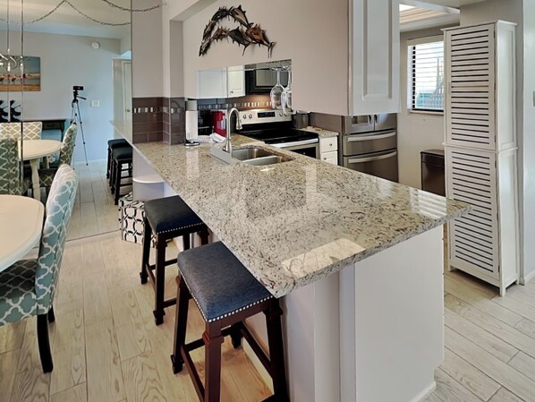 A modern kitchen with a granite island, stainless steel appliances, and a dining area with patterned chairs.