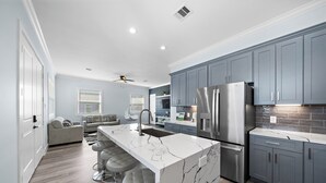 Una cocina moderna con armarios grises, una isla de mármol blanco, electrodomésticos de acero inoxidable y una zona de bar con taburetes.