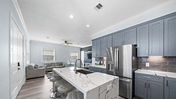 A modern kitchen with grey cabinets, a white marble island, stainless steel appliances, and a bar area with stools. - Beachside Serenity (Galveston)