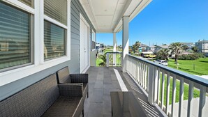 A covered porch with wicker furniture, a view of a green lawn, and a clear blue sky. - Beachside Serenity (Galveston)