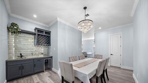 A modern kitchen with grey cabinets, a tiled backsplash, and a dining area with a table and chairs. - Beachside Serenity (Galveston)