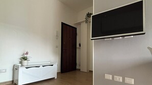 A spacious room with a wooden floor, a white bench with a potted plant, a dark door, and a mounted flat-screen TV. - Civic8-Navigli-Iulm (Milano)