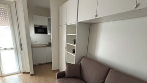 A modern living room with a brown sofa, a kitchen area with white cabinets, and a sliding glass door leading to a balcony. - Civic8-Navigli-Iulm (Milano)