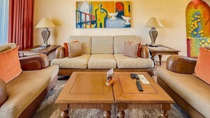 A living room with a sofa set, two side tables with lamps, a coffee table, and a colorful abstract painting on the wall. - The Royal Haciendas All Suites Resort (Playa del Carmen)