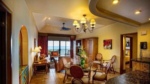 A spacious living area with a dining table, comfortable seating, a large window with a view, and a ceiling fan. - The Royal Haciendas All Suites Resort (Playa del Carmen)