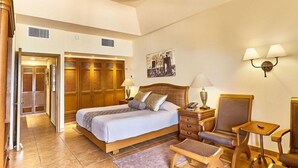 A hotel room with a bed, two bedside tables, a chair, a desk, a wardrobe, and a ceiling fan. - The Royal Haciendas All Suites Resort (Playa del Carmen)