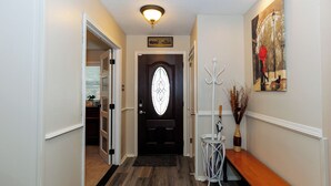 A hallway with a dark wooden floor, a black door with a glass panel, a white bench, and a wall-mounted coat rack.