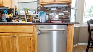 A kitchen with a stainless steel dishwasher, wooden cabinets, a tiled backsplash, and a window providing natural light.