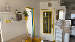 A compact living space with a sofa, a small table, a fan, and a kitchen area.
