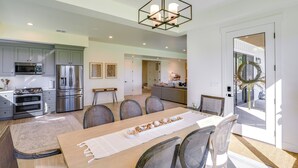 A modern kitchen with stainless steel appliances, a dining area with a long table and chairs, and a large chandelier. - Midway Mtn Retreat | Hot Tub, Gym & 28+ Nights (Midway)