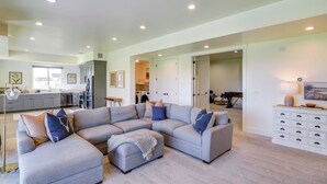 A spacious living area with a sectional sofa, a small ottoman, and a white console table. - Midway Mtn Retreat | Hot Tub, Gym & 28+ Nights (Midway)