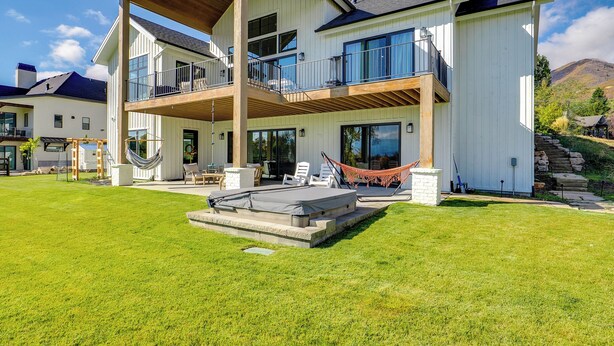 A two-story house with a balcony, a hammock, and a patio area. - Midway Mtn Retreat | Hot Tub, Gym & 28+ Nights (Midway)