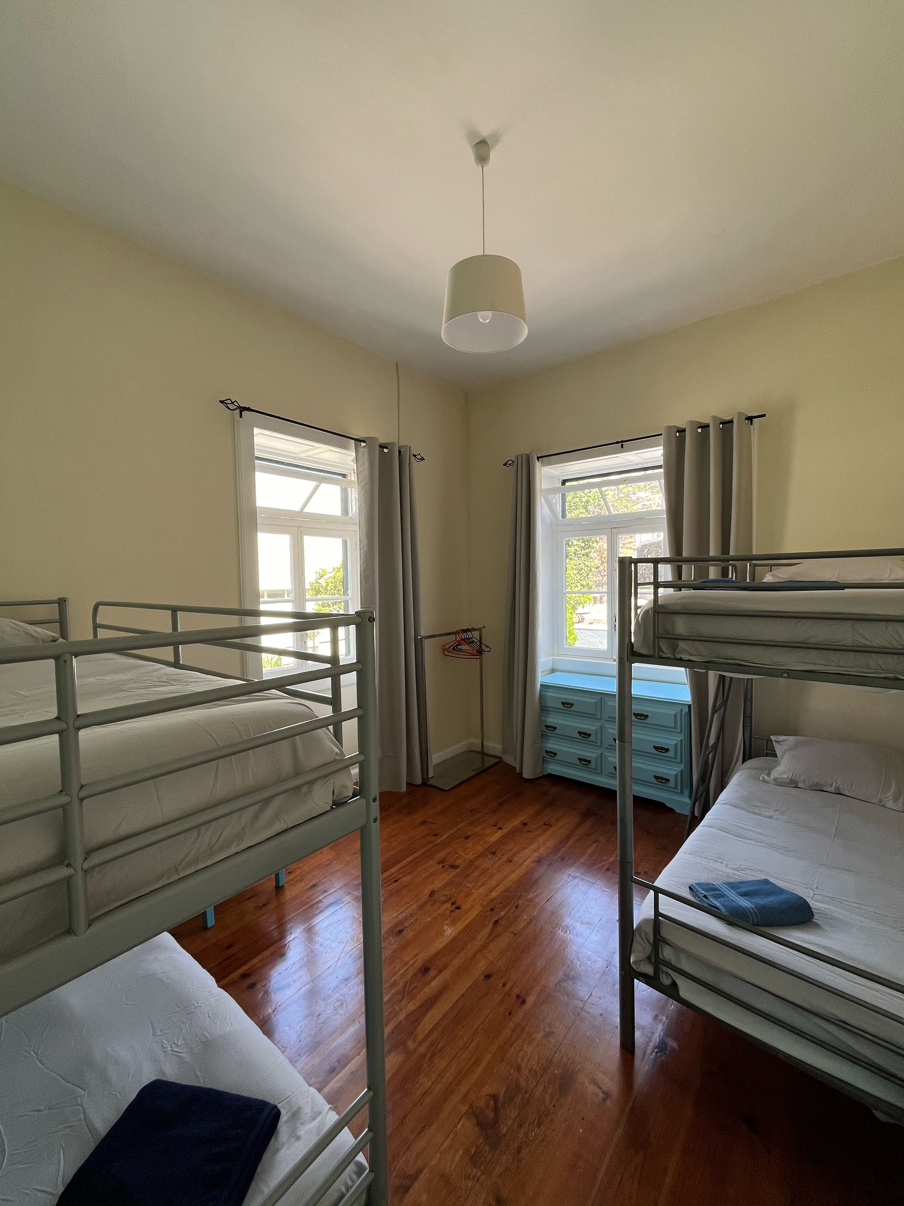 Una camera del dormitorio con letti a castello, pavimento in legno, una finestra con tende e una lampada a sospensione.