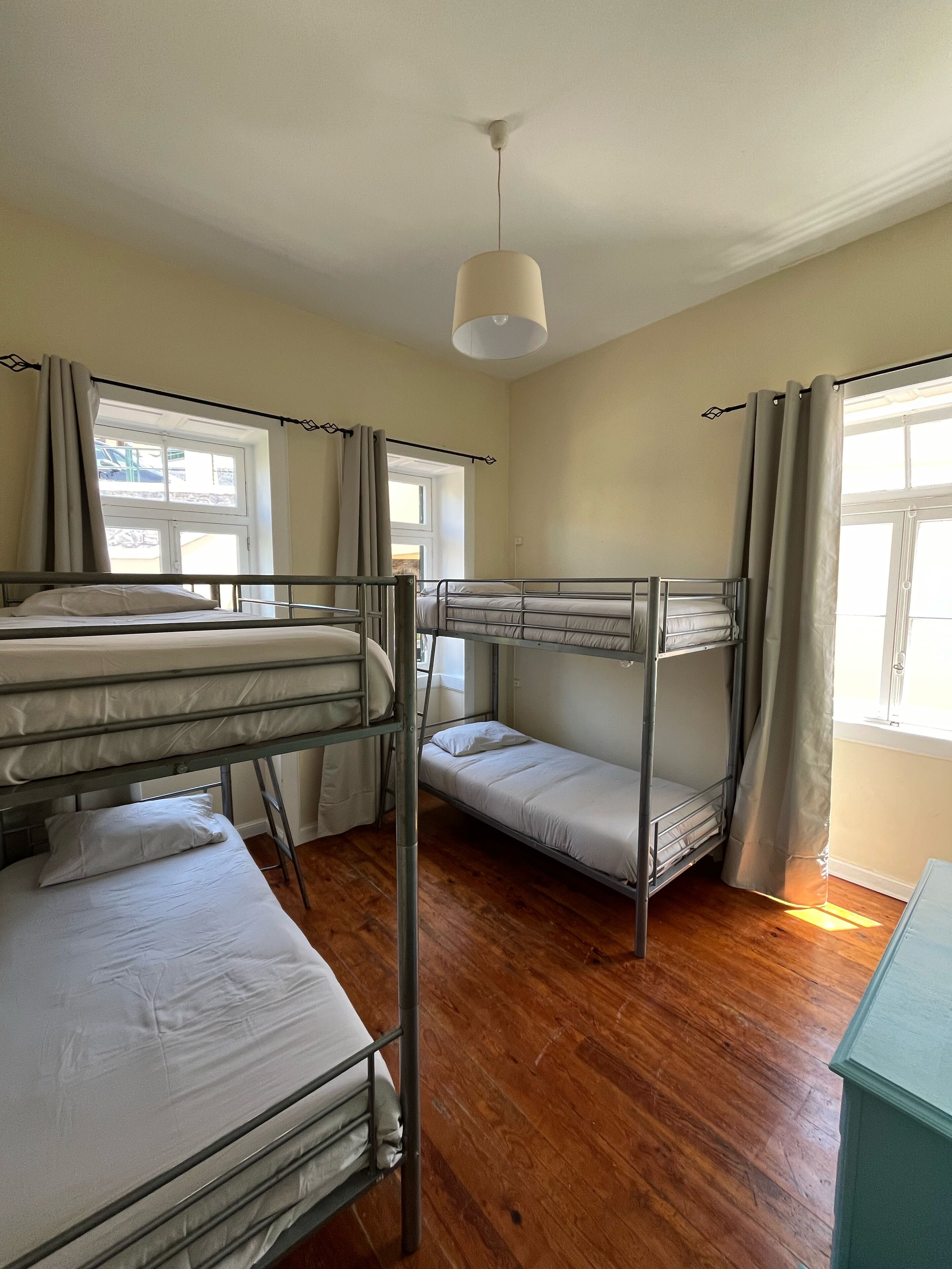 A dormitory room with bunk beds, a ceiling fan, and a window with curtains.