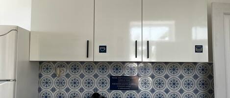 Una cocina con armarios blancos, encimera negra y salpicadero con estampado azul y blanco.